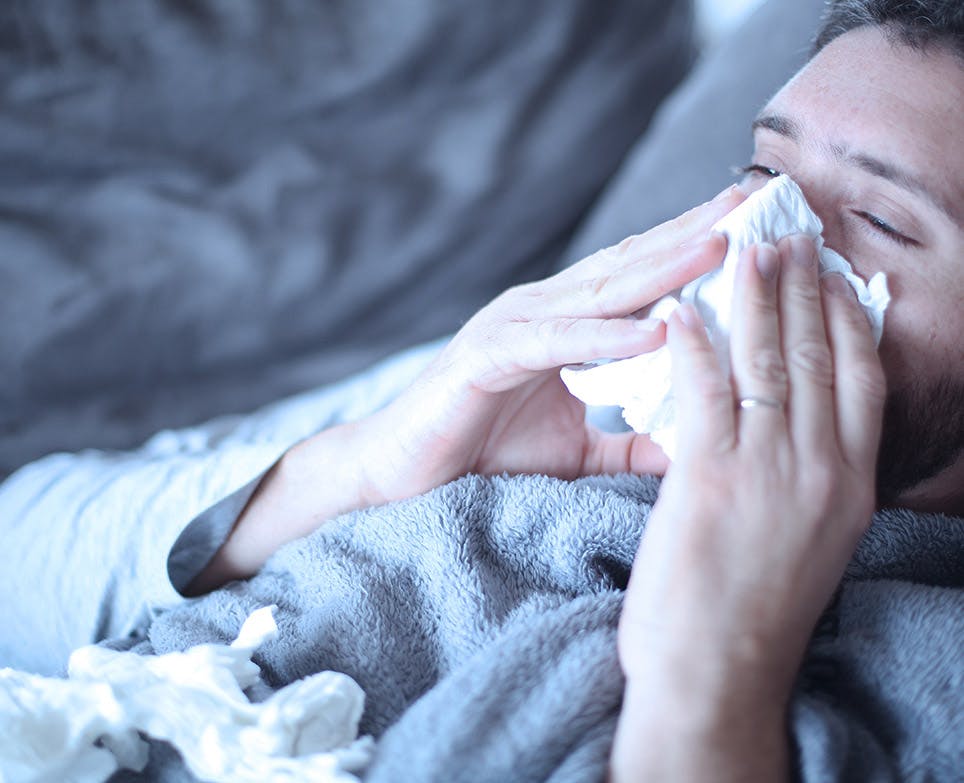 Hombre con congestión nasal limpiando su nariz, recostado en una cama. 