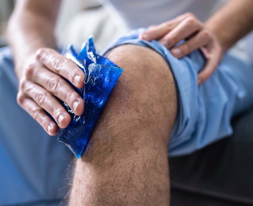 Hombre sujetando una compresa fría en su rodilla. 