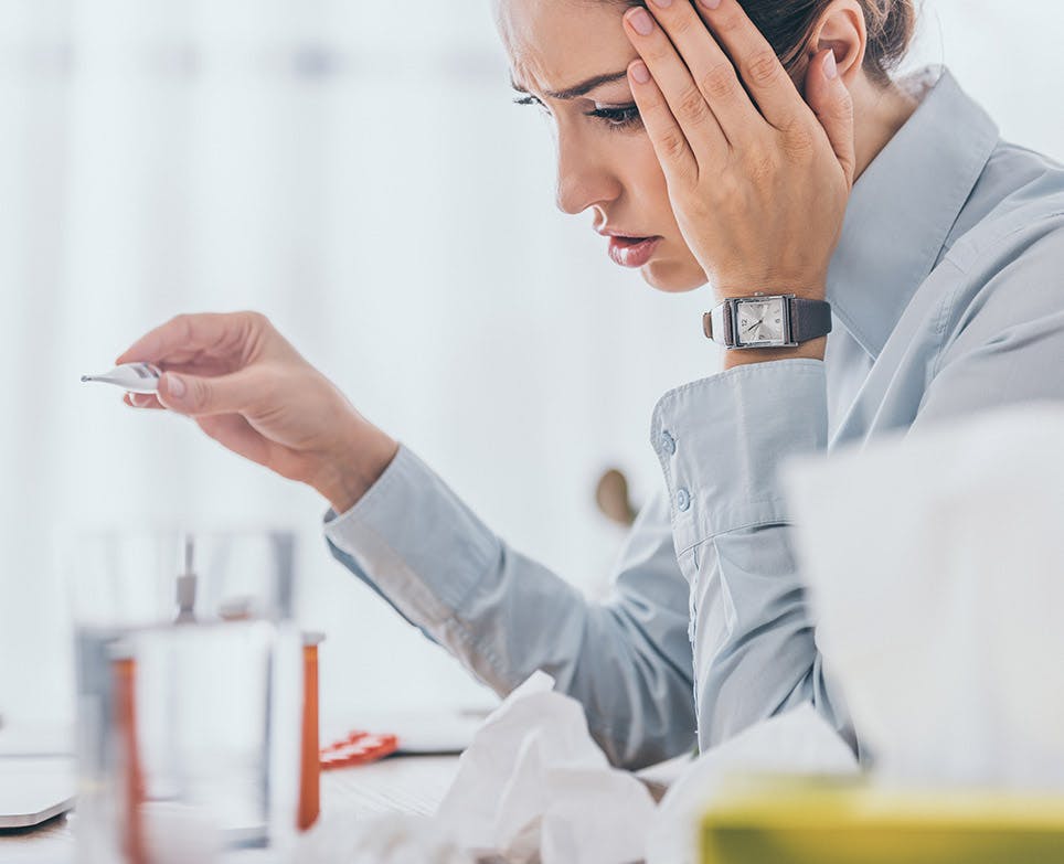 Mujer leyendo su temperatura en termómetro digital se toca la cabeza en señal de dolor. 