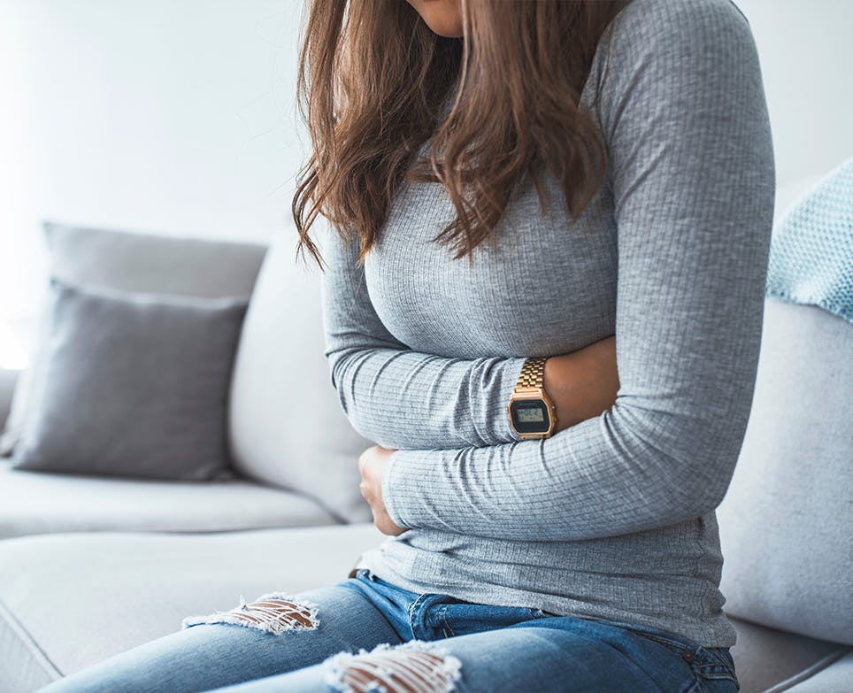 Mujer tocándose el vientre bajo con las dos manosen señal de dolor. 