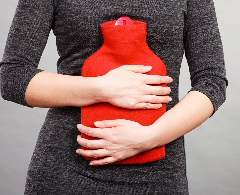 Torso de mujer sosteniendo una bolsa de agua caliente contra su vientre. 