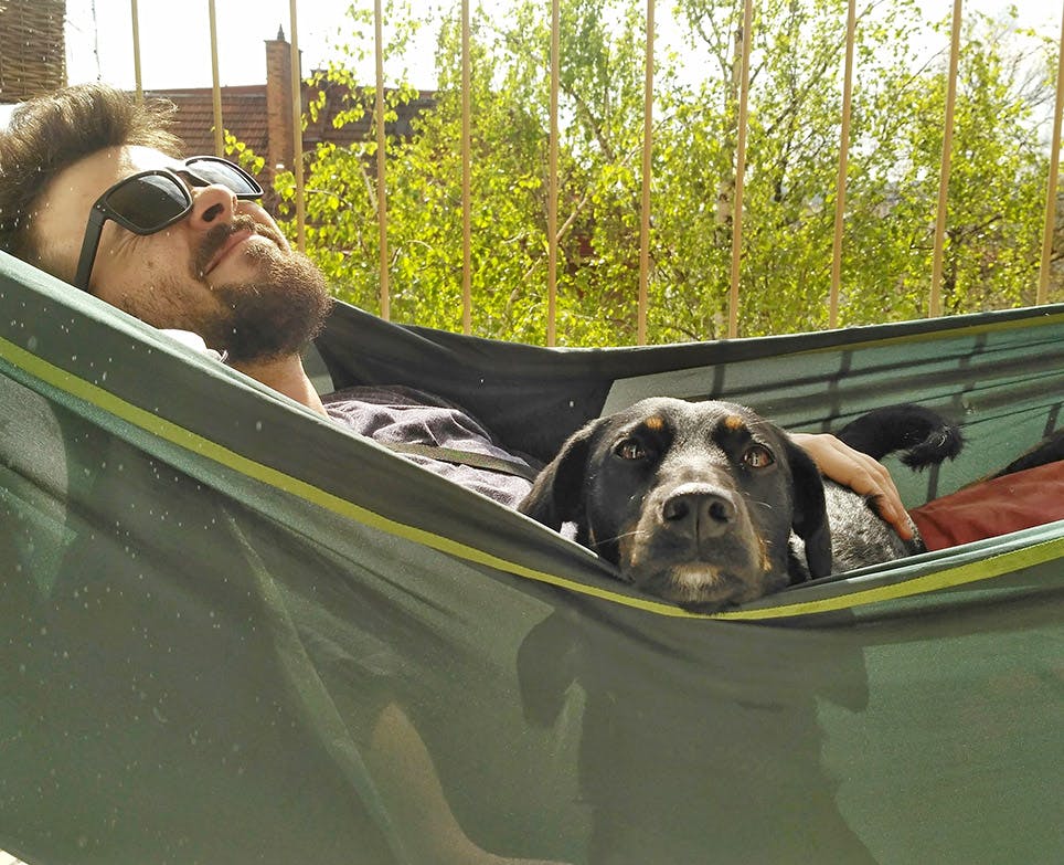 Hombre joven recostado con su perro en una hamaca. 