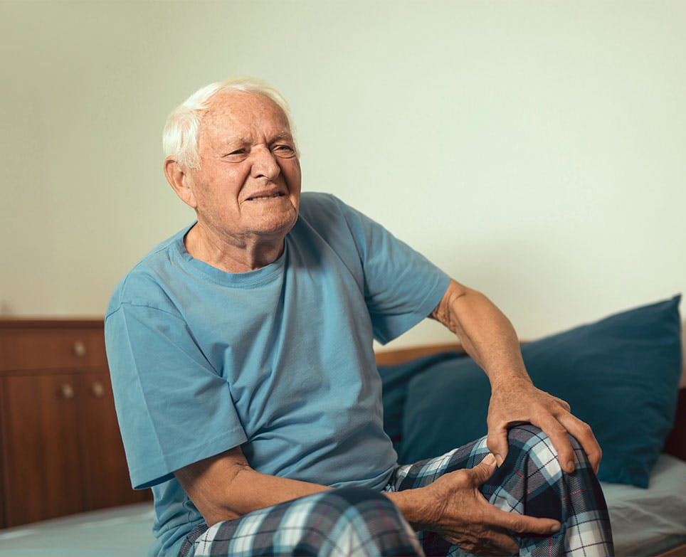 Hombre mayor toca su rodilla en señal de dolor.