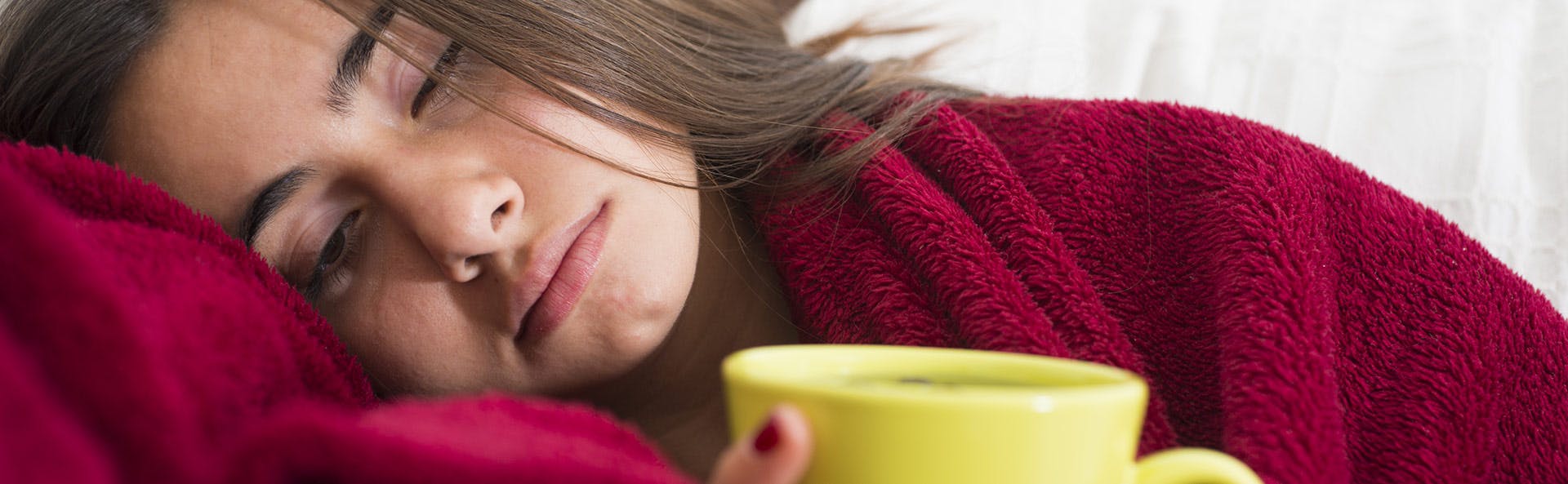 Mujer con síntomas gripales tomando una bebida caliente. 