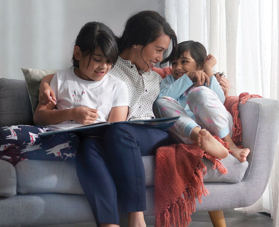 Madre con sus dos hijas leyendo un libro.