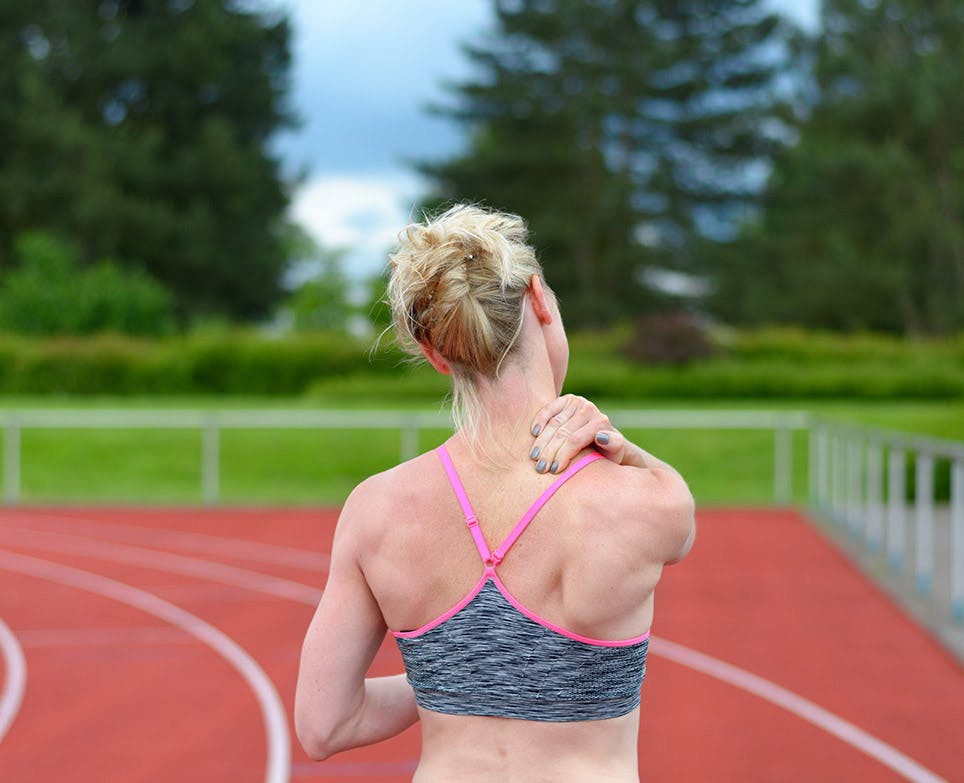 Mujer deportista toca su espalda alta en señal de dolor.