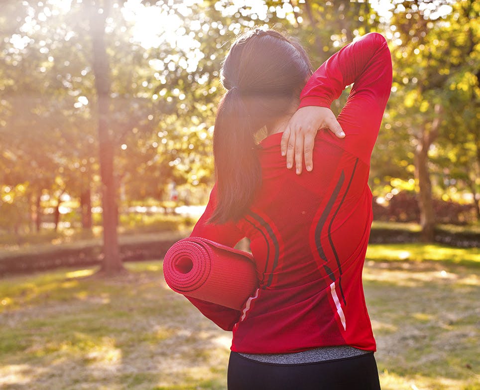 Mujer deportista al aire libre toca su espalda alta en señal de dolor.