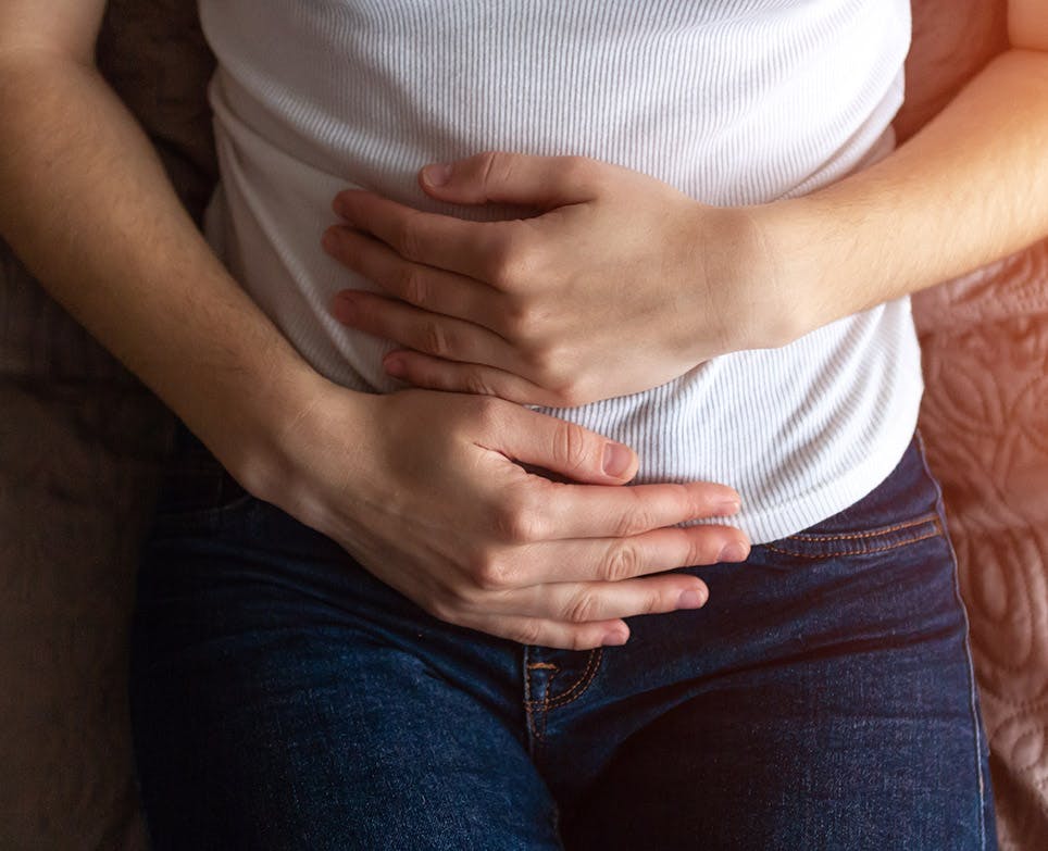 Torso de una mujer que toca su abdomen en señal de dolor.