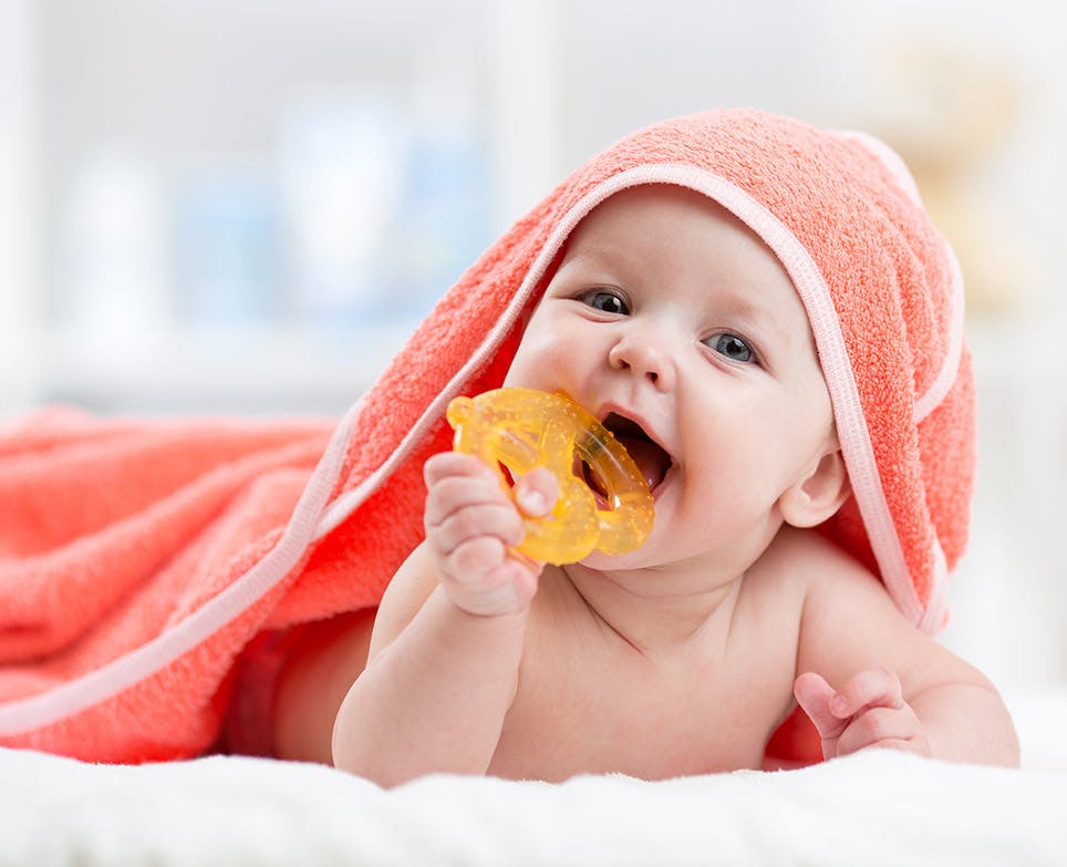 Bebé mordiendo un juguete para dentición luego de un baño.