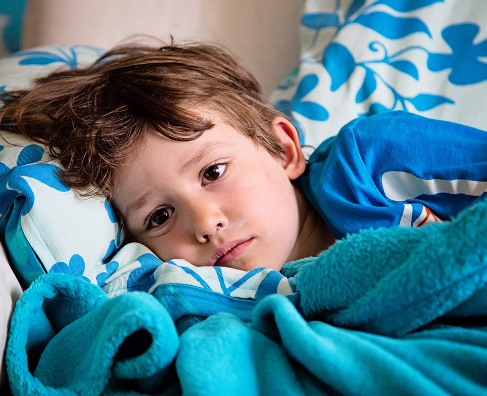 Niño recostado en su cama con síntomas de gripe.