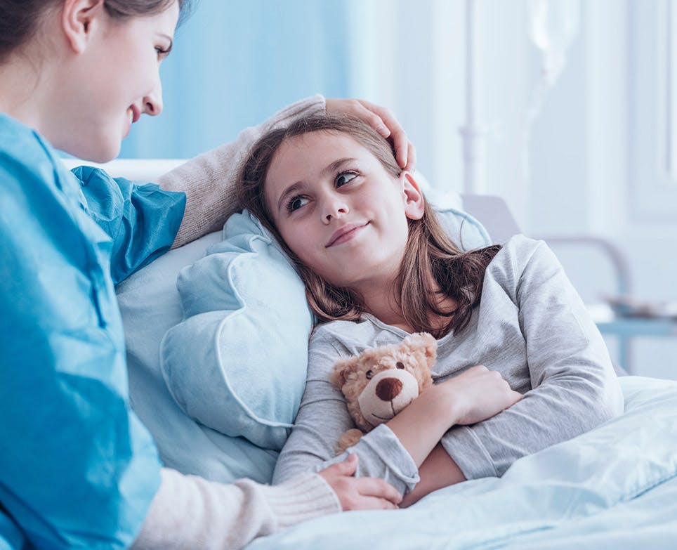 Mujer acariciando y sonriendo a una niña recostada en su cama.