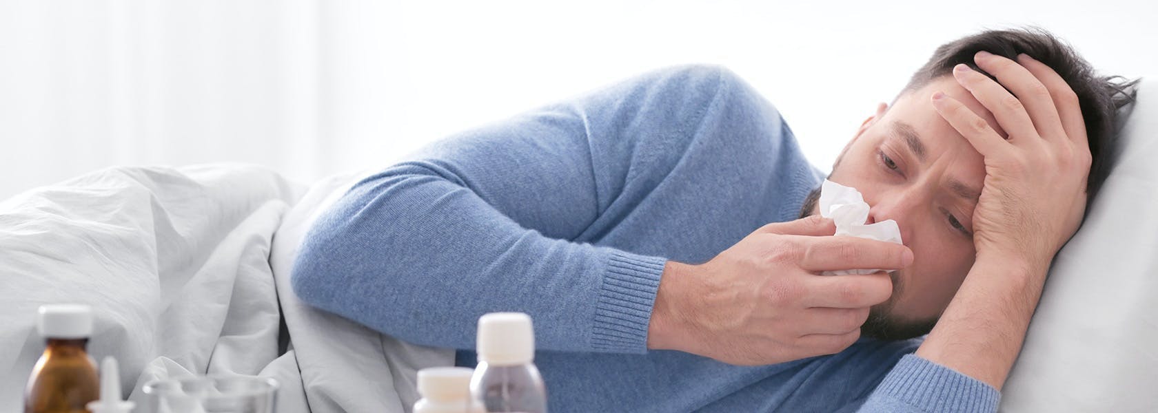 Hombre acostado en su cama con síntomas de gripe y limpiando su nariz. 