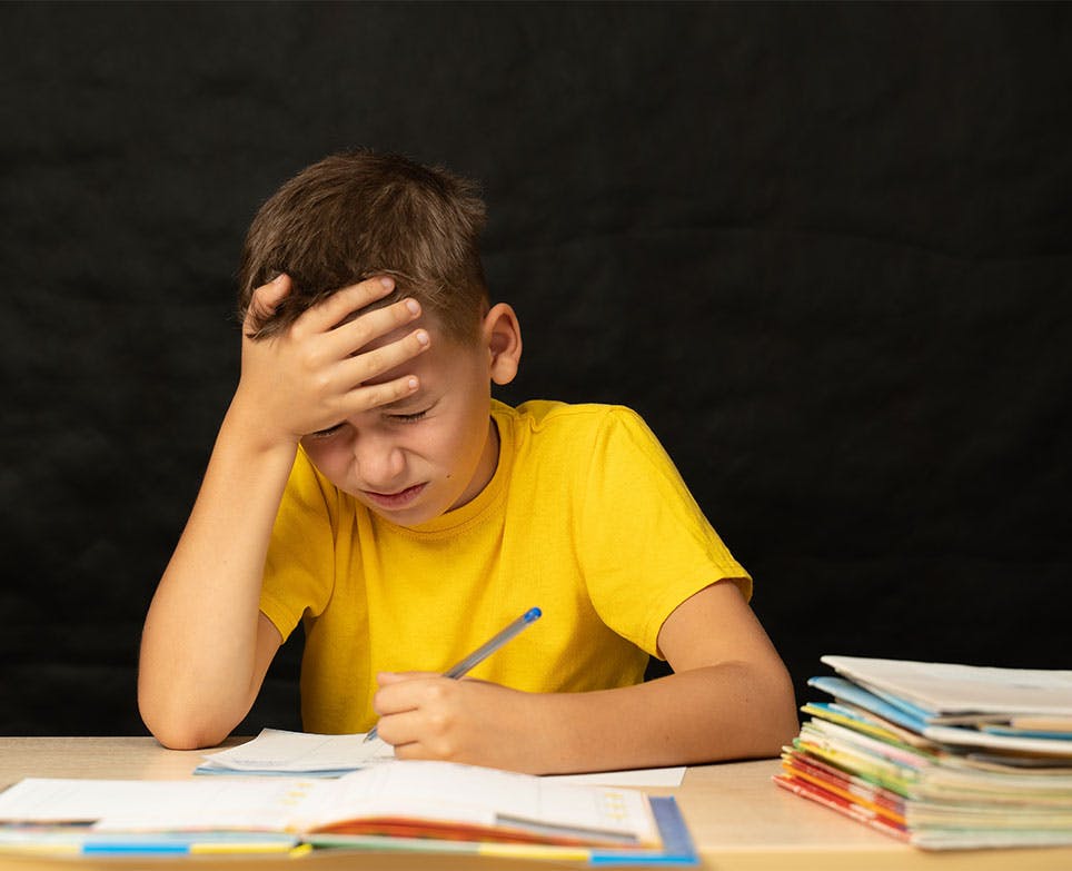 Niño se toma la cabeza en señal de dolor mientras estudia. 