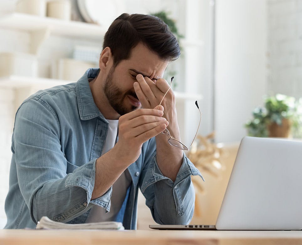 Hombre frente a un computador tomandose la frente de la cabeza en señal de dolor. 