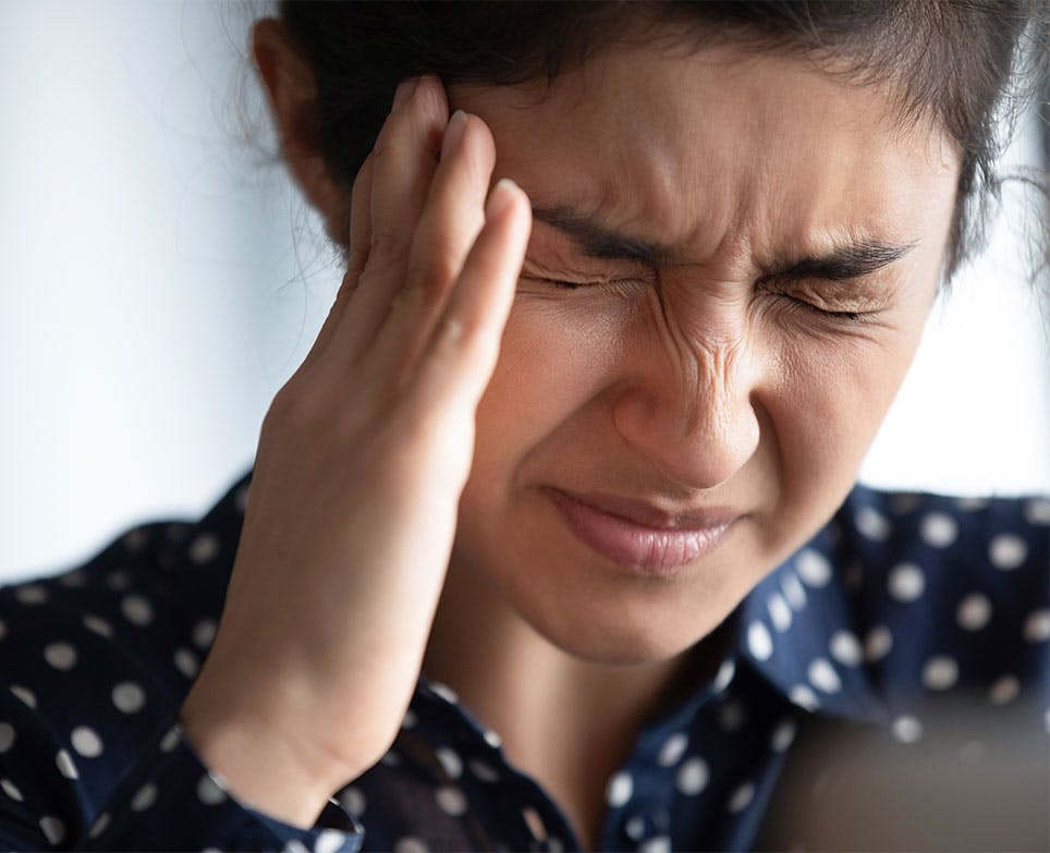 Mujer se se toca su cabeza con su mano derecha en señal de dolor. 