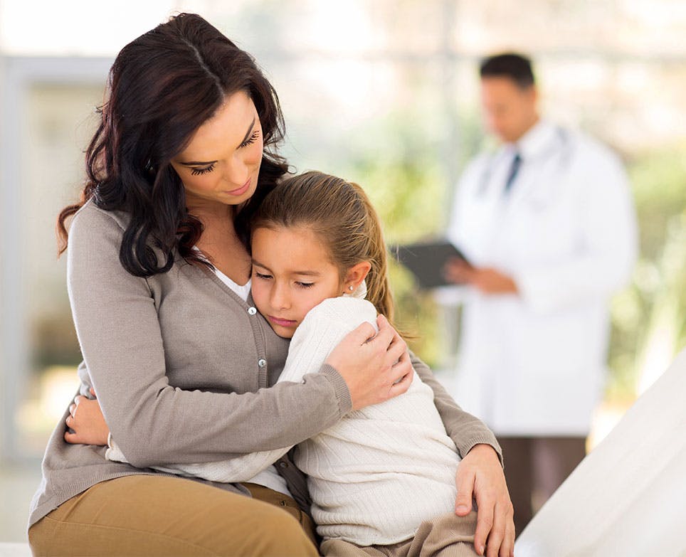 Madre abraza a su hija, al fondo se ve un doctor. 