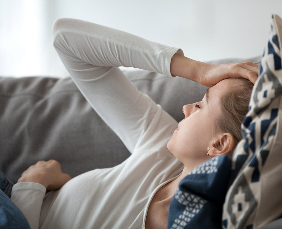 Representación de dolor de cabeza en una mujer joven, recostada, mientras se toca la cabeza 