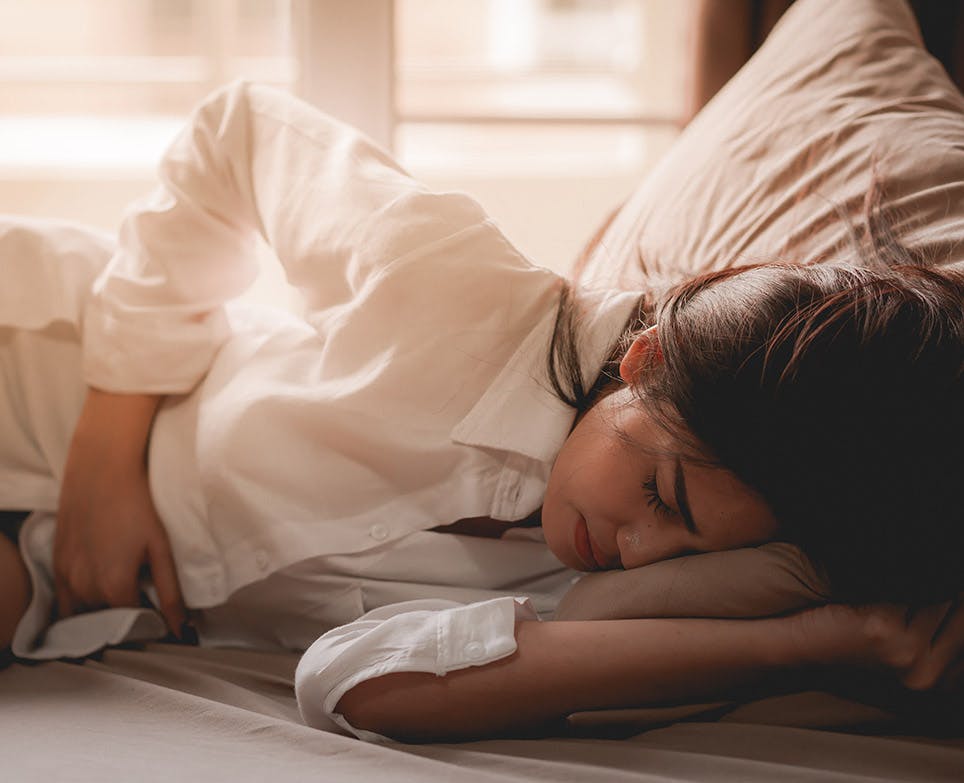 Mujer recostada en la cama tocándose el vientre bajo con la mano derecha en señal de dolor. 