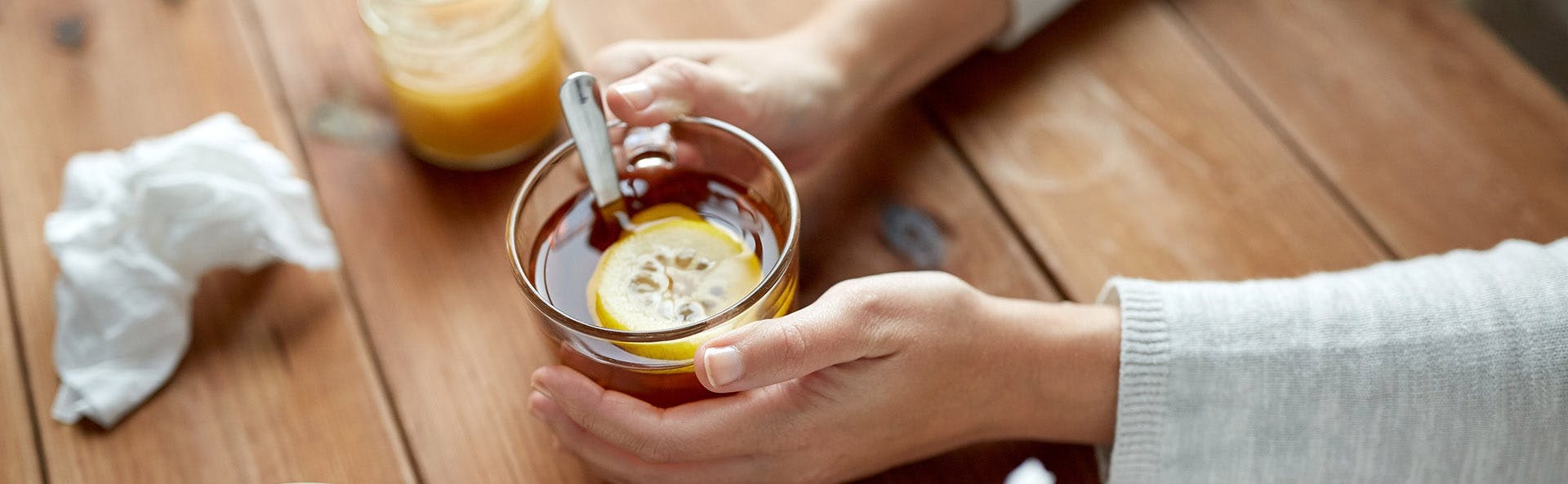 Zolben - Sobre una mesa de madera, dos manos de mujer sostienen una taza de té con una rodaja de limón 