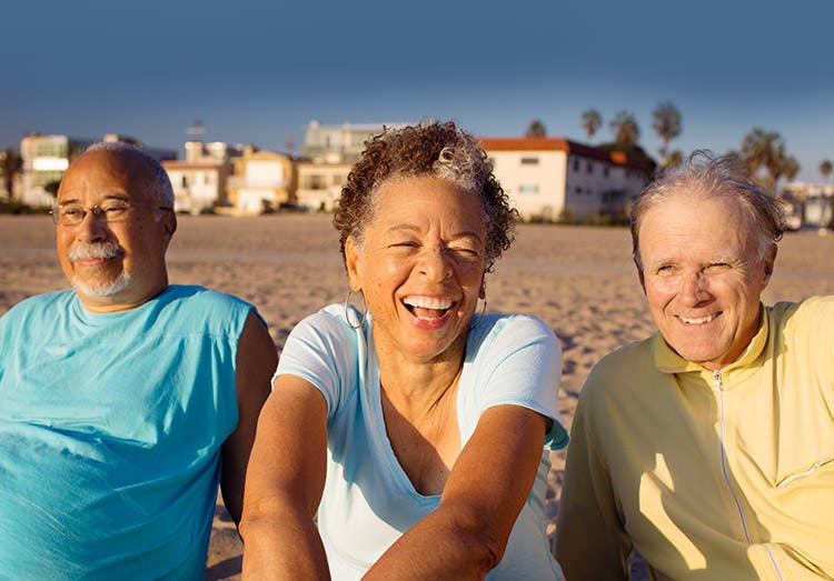 Tre ældre voksne slapper af og ler på stranden