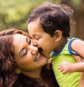 Happy Little Indian Boy Kissing Mother Outdoors