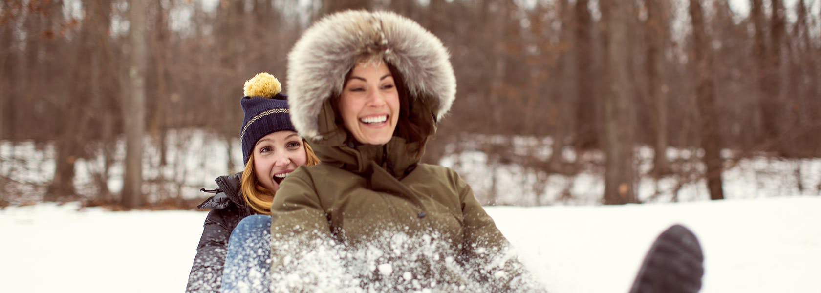 Two Women Having Fun Sledding In Woods