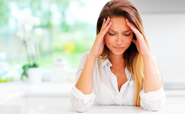 Mujer toca la cabeza con ambas manos en señal de dolor.