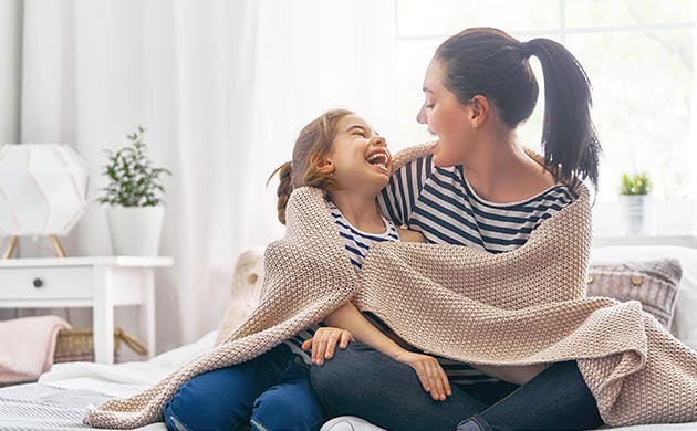 Una mamá y su hija abrazadas y cubiertas por una cobija.