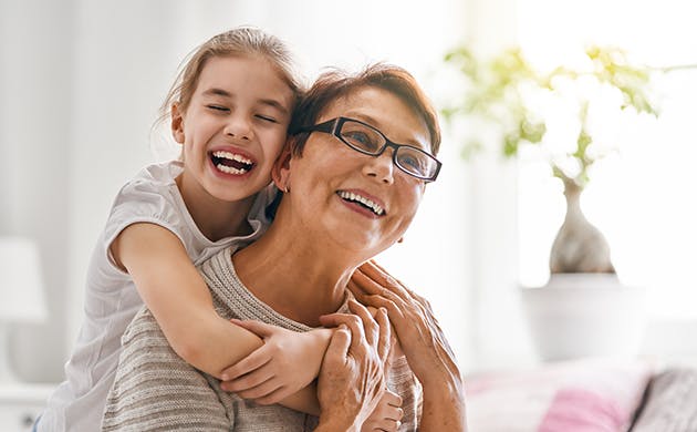 Una niña abraza a una mujer por la espalda, las dos sonríen.