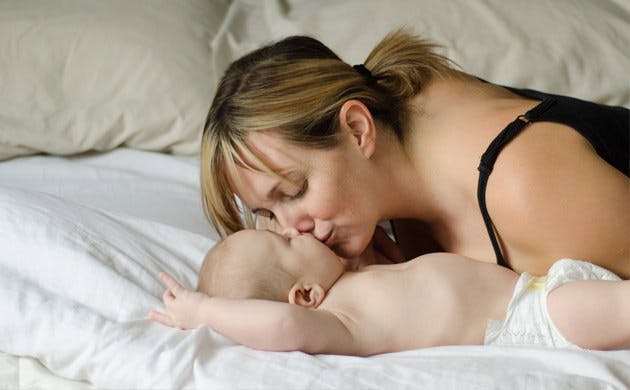 Una madre besa a su bebé mientras este descansa en la cama.