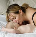Una madre besa a su bebé mientras este descansa en la cama.