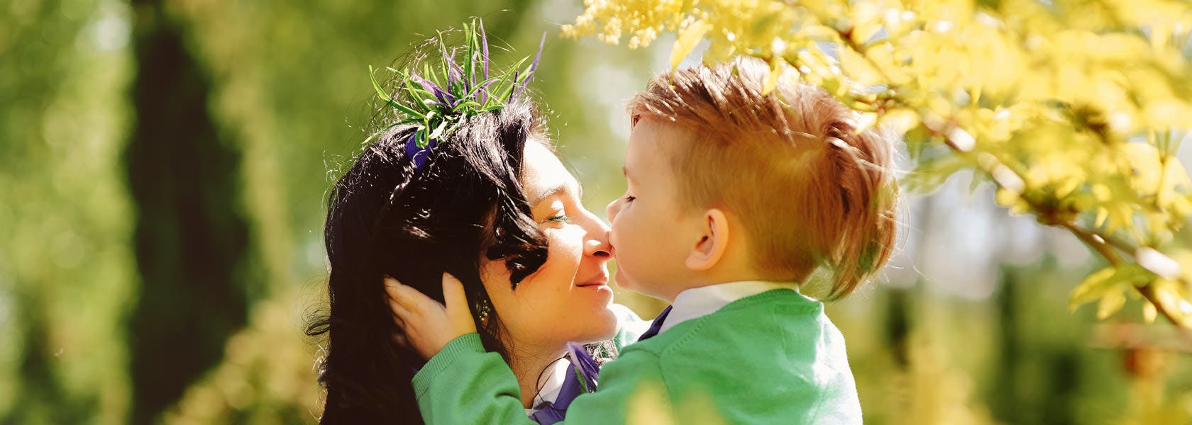 Madre e hijo al aire libre, el niño le esta dando un beso a la mamá en la nariz.