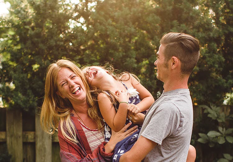 Pareja de padres jugando con su hija al aire libre.