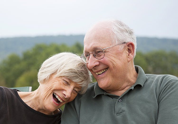Una pareja de adultos mayores sonríen, sentados en un parque.