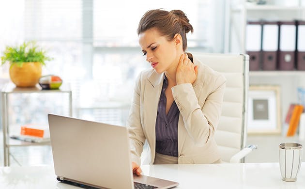 Una mujer toca su cuello en señal de dolor mientras trabaja frente a un portátil.