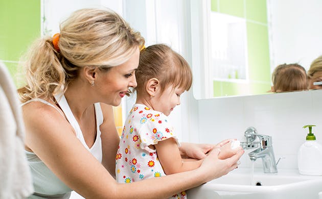 Una mamá le ayuda a su hija a lavarse las manos.
