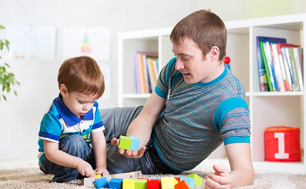 Un padre juega con su hijo pequeño en una habitación.