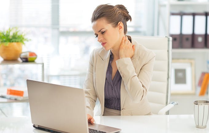 Mujer al frente de un computador portatil tocandose el cuello de dolor