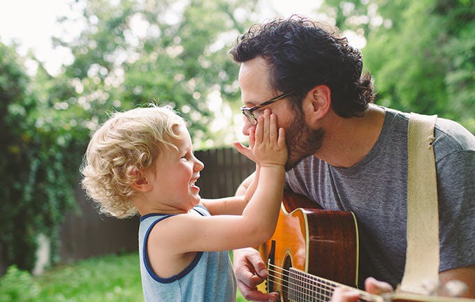Un papá toca la guitarra para su hijo mientras éste le acaricia la cara.