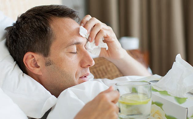 Hombre con sintomas gripales recostado en la cama tocandose la cabeza con señal de dolor