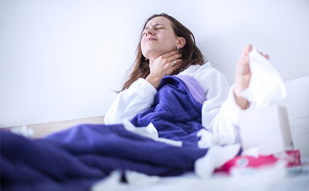 Una mujer con síntomas gripales toca su garganta por señal de dolor.