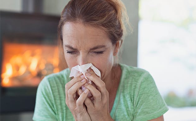 Mujer con síntomas gripales sonándose la nariz.