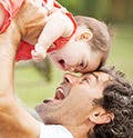 Un papá carga a su hijo bebé mientras los dos ríen.