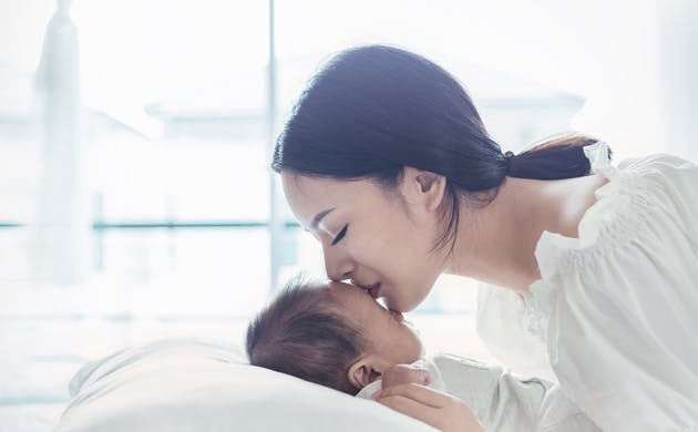 Mom Giving Kiss To Baby On Soft Bed
