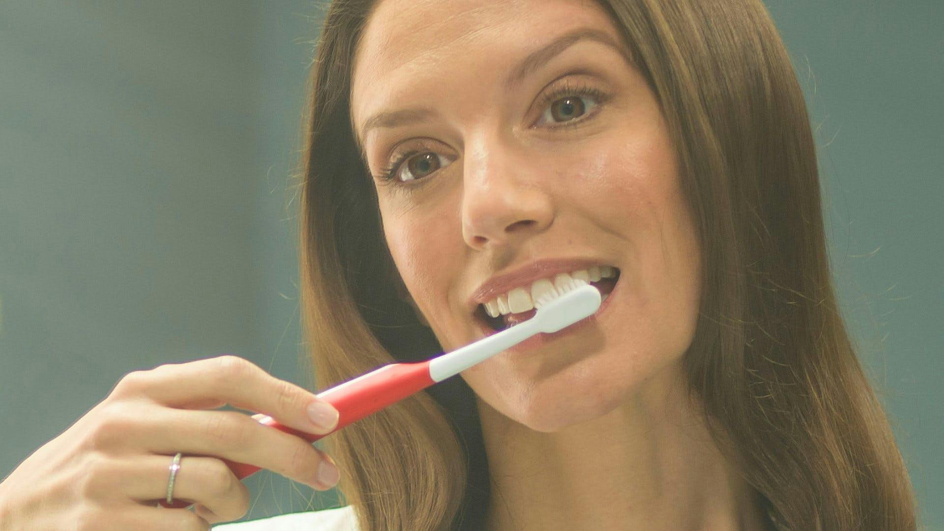 Mujer mirando al lavabo agarrando un cepillo de dientes