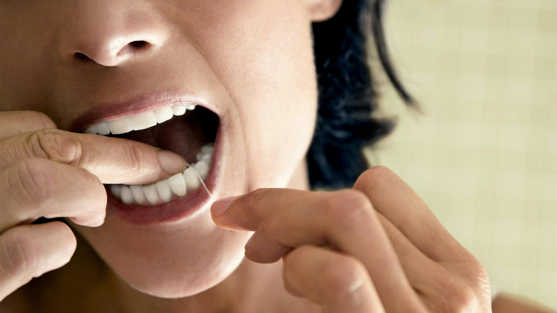 woman using dental floss to clean between teeth