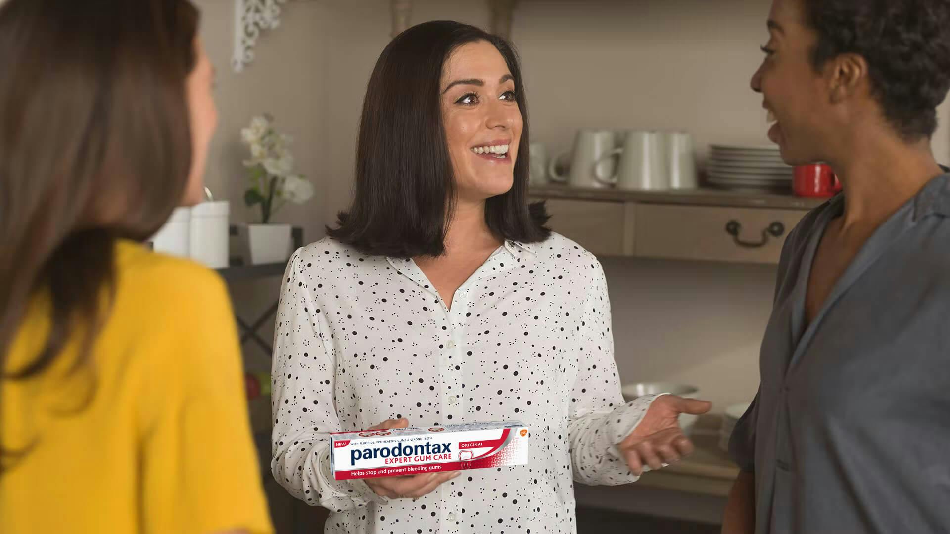 A woman smiling and talking to others while holding toothpaste