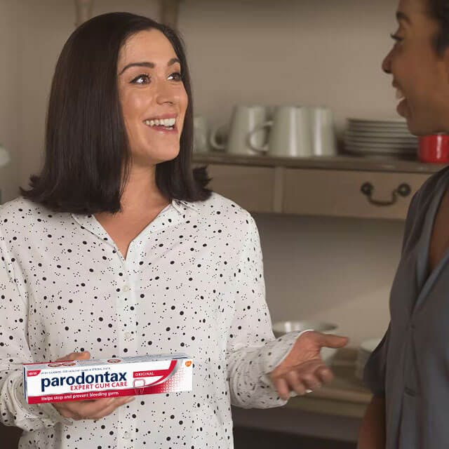 A woman smiling and talking to others while holding toothpaste