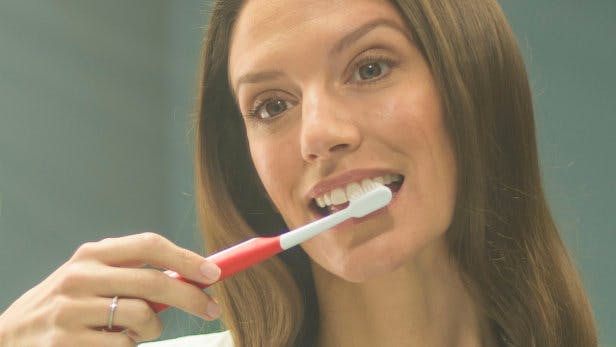 Une femme qui saigne des gencives et qui tient une brosse à dents 