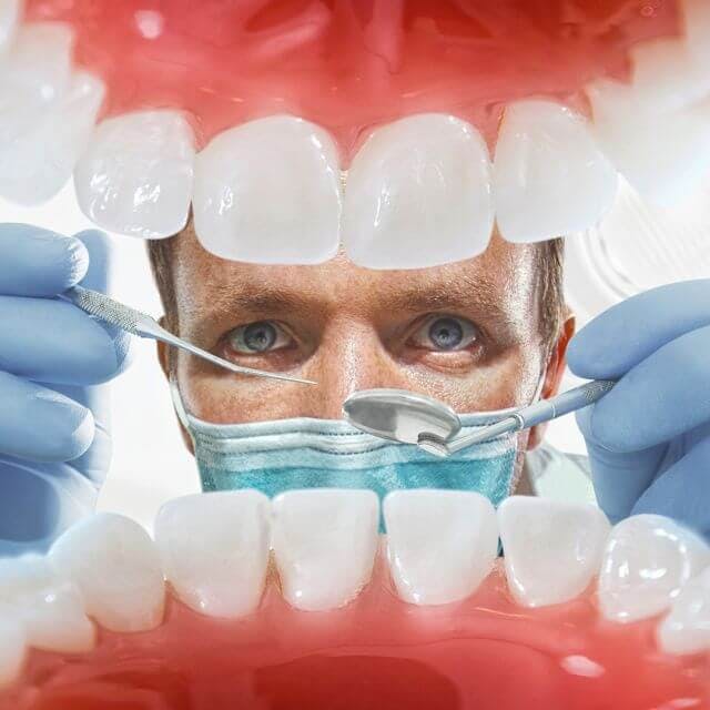 A dentist looking in someones mouth with tools. 